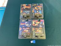 Four 1990s vintage KISS themed Johnny Lightning Racing Dreams matchbox cars in original blister packaging placed on green fabric.