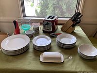 Full view of dinnerware, toaster, knife block, can opener, and butter dish on table near window.