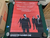 Photo showing entire Gangster Number One movie poster laid flat with weights at corners for display.