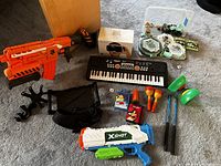 Full lot overview including two Nerf toy blasters, electronic keyboard, wallets, Qixels, maracas, kendama ball game, and mini iPad holders.