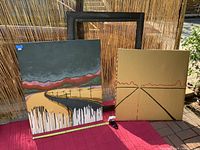 Two paintings displayed side by side with large black wood frame behind on red cloth and bamboo background outdoors