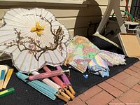 Photo showing four vintage paper umbrellas with painted branch and flower designs and several folded sheets and blankets with colorful floral and grannycore patterns.