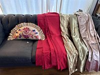 Image showing the semicircle gold embroidered pillow on the left and the red silk curtain panels and assorted gold, dark gold, and rose gold fabrics on the right, arranged on a couch.