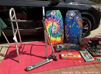 Wide view showing Razor scooter, aluminum zimmer frame, two colorful bodyboards, Star Wars Monopoly game and assorted toys laid out on red mat