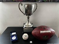 Photo of all four items in the lot: NFL football, baseball, stopwatch in box, and silver sports trophy.