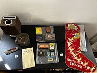 Full view of lot showing all items including cork tissue box cover, metal cup, folding knife, guest check booklet, Christmas stocking, matchboxes, Zippo lighter, and labels.