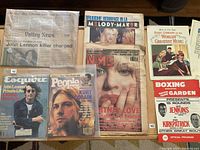 Photo showing a collection of magazines, newspapers, and programs including 1980s LA Valley News newspaper about John Lennon, Esquire magazine, People magazine with Kurt Cobain, NME magazine with Britney Spears, boxing program, and a music book.