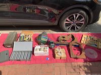 Complete lot including wooden child's tool kit laid out, multicolored glass lantern, several illustration markers in a box, smaller metal lantern, and round glass slide tray on red cloth on pavement