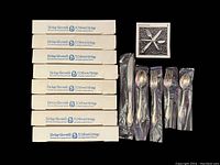 Eight rectangular white boxes labeled Heritage Silversmiths stacked, five additional flatware pieces in plastic wrappers and a small decorative sticker.