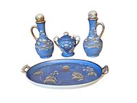 Front view of the complete set showing two cruet bottles, lidded jar, and platter with blue background and gold-white Japanese motifs.