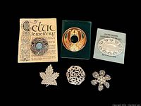 Six vintage brooches arranged together on black background showing Celtic, enamel, mother of pearl, rhinestone, and floral designs; also includes two vintage display cards for the Celtic and mother of pearl brooches.