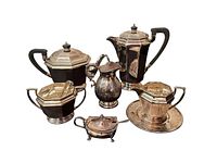 Full grouping of the nine-piece vintage silver-plated tea set including teapot, coffee carafe, creamer with plate, sugar bowl with tongs, cruet dish with spoon and tall lidded creamer.