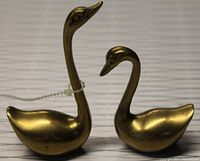 Front and side view of two brass swan figurines showing height difference and details.