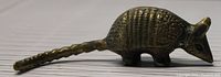 Side angle showing detailed scales on the shell and elongated tail of the brass armadillo figurine.