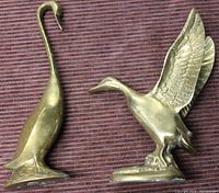 One photo showing both brass bird figurines on a textured surface, highlighting the standing crane/heron and the bird with raised wings.