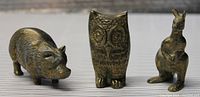 Front view of brass pig, owl, and kangaroo figurines together on a flat surface