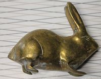 Side view close-up of brass rabbit figurine, showing patina and wear on surface