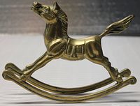 Side view of the brass rocking horse figurine showing horse head, body, saddle, and rocker base.