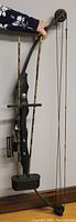 Full view of black Jennings compound bow mounted on wall showing bowstring, pulley, foot stirrup, and attached cables.
