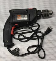 Full image of the black Skil Slugger electric drill with red trigger, showing the cord and plug wrapped around the tool.