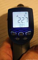 Front view of infrared thermometer in use showing digital LCD screen displaying temperature 22.7°C with various mode and function buttons below the screen.