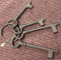 Four used metal skeleton keys attached to a metal ring, shown on a textured surface.