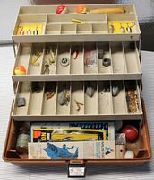 Fishing tackle box open showing fishing lures, bobbers, hooks, sinkers, and accessories inside compartments
