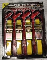 Photo of unopened package containing four 1" x 10' yellow ratchet tie downs with red hooks and ratchet mechanisms. Package labeling shows 900 lbs load rating.