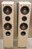 Front view of the pair of Technics SB T200 speakers showing two woofers with metallic centers, one tweeter between, and a bass port at the bottom front of each speaker. Light wood finish cabinets.
