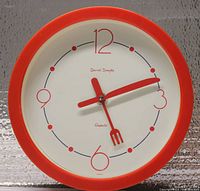 Front view of Daniel Dakota red quartz kitchen wall clock with white dial, red frame, and utensil shaped hands.