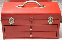 Front view of the red metal toolbox showing silver handle, clasps, and bottom drawers with pull knobs.