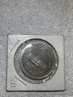 Canadian silver-colored $1 coin in cardboard holder, front side showing building and inscriptions.