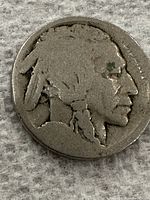 Close-up photo of the obverse side of a heavily worn Buffalo nickel featuring a Native American profile, showing signs of heavy circulation.