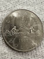 Obverse side of 1980 Canadian dollar coin showing Voyageur canoe scene with two paddlers, trees, and 'CANADA DOLLAR 1980' inscriptions.
