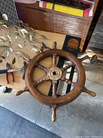 Full view of the wooden ship steering wheel showing the circular rim, six wooden spokes, and brass center hub.
