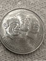 Close-up image of the front side of the Apollo 11 Canadian commemorative token showing the relief portraits of astronauts Aldrin, Armstrong, and Collins with inscriptions.