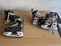 Pair of black and grey Bauer youth hockey skates on a wooden surface, side view.
