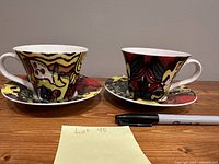 Front view of two contemporary Picasso tea cups on matching saucers, with a Sharpie marker for size comparison