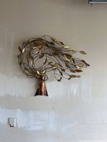 Full view of the copper tree wall art hung on a wall showing the metal trunk and branches with gold-toned leaves in a circular design.