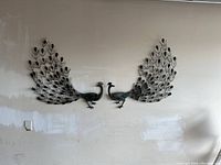 Wide shot of two copper peacock wall arts mounted side by side with tails fanned out.