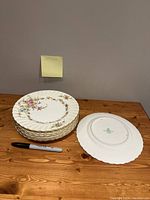 Stack of 8 Minton fine English china salad plates with floral design and gold trim, scalloped edges, with memo note LOT 104 and marker for size comparison