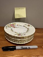 Eight vintage Minton Lorraine pattern fine English china plates stacked with an 8-sided shape, floral decoration, and gold trim visible on edges. Sharpie marker placed for size comparison.