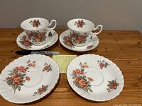 Two tea cups and two matching saucers, plus two additional saucers arranged with a marker for size reference on a wood table