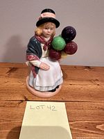 Full view of Royal Doulton Balloon Girl figurine showing seated girl holding balloons on a wooden surface with "LOT 42" note.