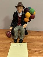 Front and side views of Royal Doulton Balloon Man figurine seated with colorful balloons and bag.