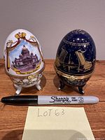 Two vintage egg-shaped trinket boxes on tripod legs, white and dark blue, placed side-by-side with a black Sharpie pen for size reference.