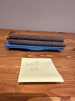 Full view of the blue model train logging car carrying three brown logs tied in a bundle on a wooden surface with a sticky note labeled 'LOT 114'.