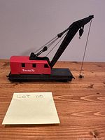 Full view of the vintage Santa Fe model train crane car showing red body and black crane on wooden surface.