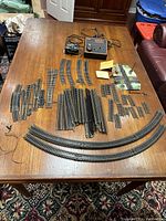 Overview of all model train track pieces laid out on wooden table including curved and straight rails, switches, and power pack controller.