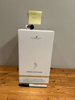 Front view of Young Living Ember Diffuser box with marker for size comparison and lot number note, showing unopened packaging.